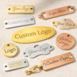 Collection of custom metal logo tags in various shapes, materials, and finishes including gold, silver, and rose gold hardware nameplates