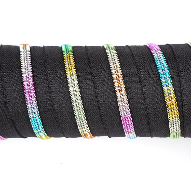 Bulk roll of #5 rainbow nylon coil zipper by the yard showing multi-color metallic gradient teeth on black polyester fabric tape.