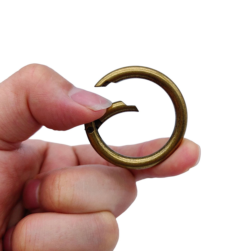 Hand demonstrating the quick release functionality of an antique brass round gate ring for leathercraft.