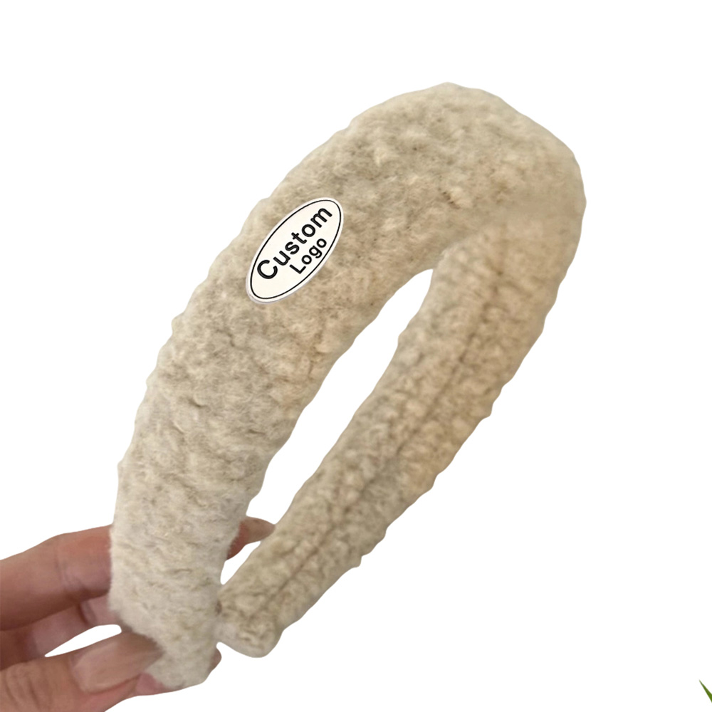 Curved metal labels for hair accessories mounted on a cream textured plush headband from small metal logo charms supplier.